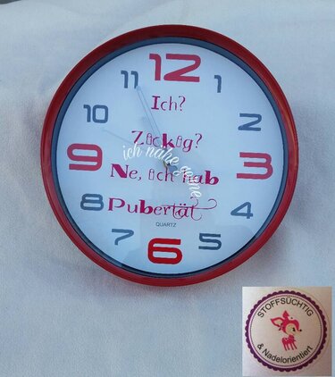 Runde Wanduhr mit rotem Rahmen, rote Ziffern bei 12/3/6/9 und Schriftzug 'Ich? Zickig? Ne, ich hab Pubertät.' in Rot und Grau.