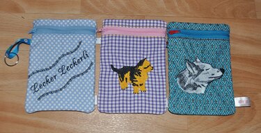 Drei bestickte ITH-Taschen mit Reißverschluss: hellblau mit Schriftzug „Lecker Leckerli“, lila kariert mit Hundewelpe, türkis mit Wolfskopf.