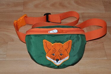 Grüne Bauchtasche mit orangefarbenem Gurt und Reißverschluss sowie Fuchskopf-Stickmotiv auf der Vorderseite.