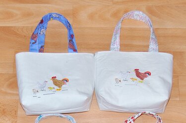 Zwei weiße Stofftaschen mit Hühner-Stickerei (Hahn, Henne, Küken).