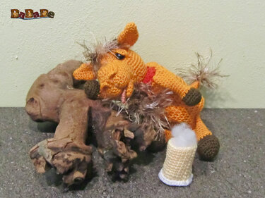 Gehäkeltes orangefarbenes Pony mit flauschiger Mähne auf Treibholz neben einer kleinen gehäkelten Deko-Kerze