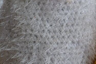 Nahaufnahme einer flauschigen weißen Häkeltextur mit langen, zarten Fasern und erkennbaren Maschen.