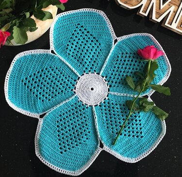 Gehäkeltes türkis-weißes Deckchen in Blumenform mit weißem Zentrum und einer rosa Rose darauf