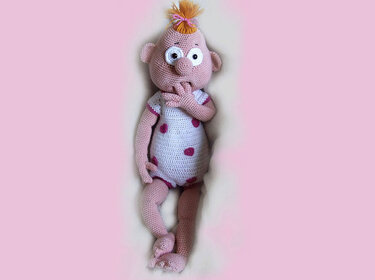Rosa Amigurumi-Puppe mit weißem Strampler, pinken Punkten und orangefarbenem Haarschopf, mit großen, ausdrucksvollen Augen.