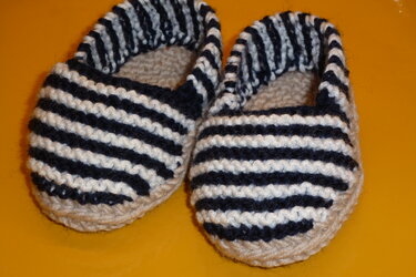 Gestrickte Babyschuhe blau-weiß gestreift auf gelbem Hintergrund