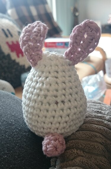 Nahaufnahme eines gehäkelten weißen Hasen mit rosa Ohren und rosa Schwänzchen.