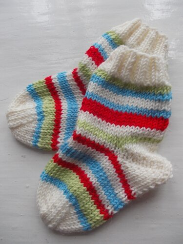 Gestrickte Babysocken weiß mit roten, hellblauen und hellgrünen Streifen