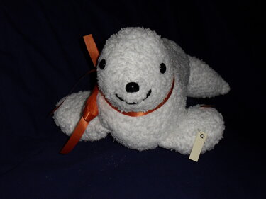 Weißer Amigurumi-Seehund mit oranger Schleife, schwarzen Augen und lächelndem Mund