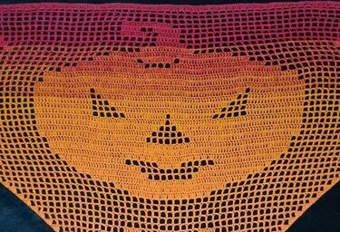 Dreieckiger Filethäkel-Schal mit stilisiertem Kürbisgesicht und Ombré-Farbverlauf von Dunkelrosa zu Orange