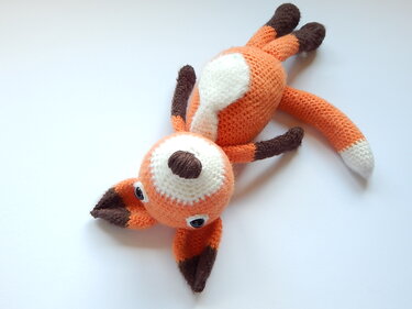 Gehäkelter Amigurumi-Fuchs liegend, orange mit weißem Bauch und braunen Pfoten