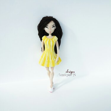Amigurumi crochet doll with dark hair wearing a yellow and white striped dress and white shoes on a white background.