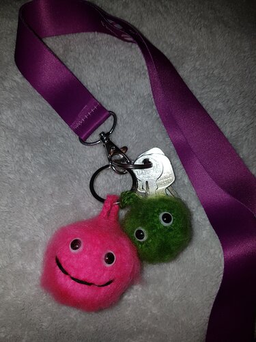 Flauschige pinke und grüne Pompon-Anhänger mit Augen an einem Schlüsselring und lila Band
