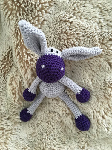 Nahaufnahme eines gehäkelten Amigurumi-Häschen mit sichtbarer Maschenstruktur, langen Ohren und lila Farbakzenten