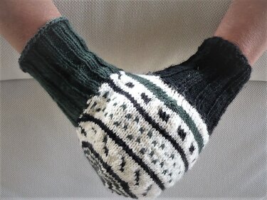 Zwei gestrickte Fausthandschuhe in Dunkelgrün, Creme und Schwarz mit nordischem Muster an Händen getragen.