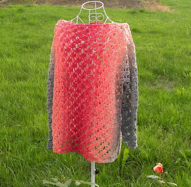 Gehäkelter Damenpullover mit rot‑grauem Farbverlauf auf Drahtbüste vor grüner Wiese