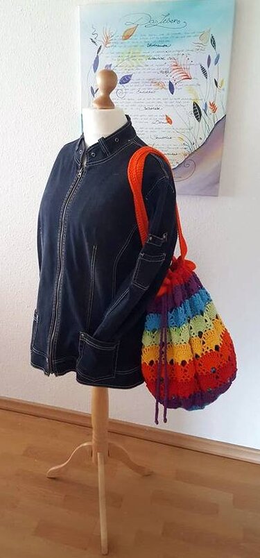 Gehäkelter Beutelrucksack in Regenbogenfarben an einer Schneiderpuppe mit schwarzer Jacke