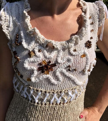 Ausschnitt eines weiß-beigen gestrickten Damenkleids mit Rüschen und Perlenapplikation