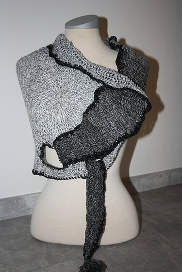 Gehäkeltes Tuch in Grau und Schwarz auf einer Schneiderpuppe mit rundem Muster und langem Bindeband.