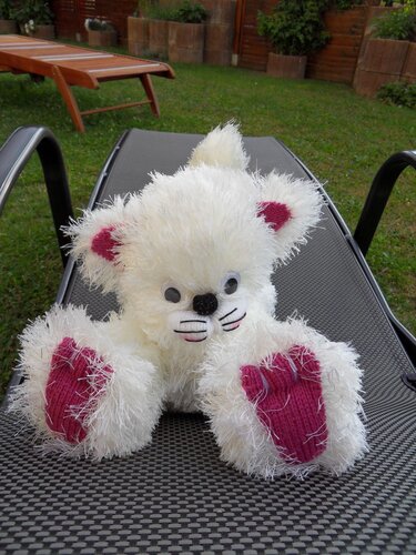 Weißes flauschiges Amigurumi-Tier mit pinken Ohren und Pfoten auf Gartenliege