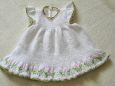 Weißes gestricktes Babykleid mit rosa-grüner Blumenbordüre am Saum