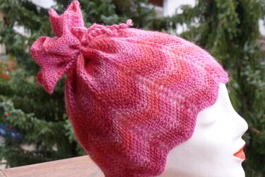 Rosa gestrickte Kinder-Mütze mit gewelltem Saum und Zierknoten auf weißem Kopfmodell