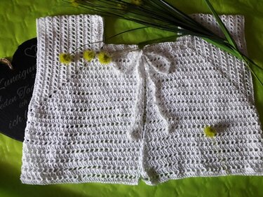 Weißes gehäkeltes Bolero-Jäckchen mit Lochmuster und Schleife auf grünem Hintergrund