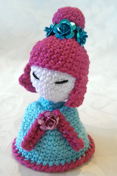 Gehäkelter Puppen-Eierwärmer mit rosa Mütze, türkisfarbenem Kleid und Blütenverzierung