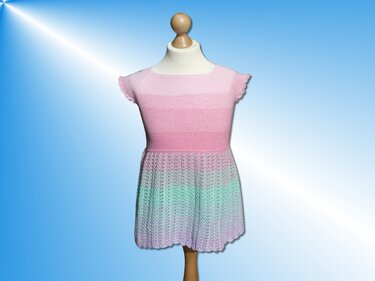 Gehäkeltes Kinderkleid in Pastellrosa, Mint und Flieder auf einer Schaufensterpuppe vor hellblauem Hintergrund