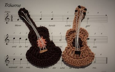 Zwei gehäkelte Gitarren-Schlüsselanhänger in dunklem und hellem Braun auf einem Notenblatt