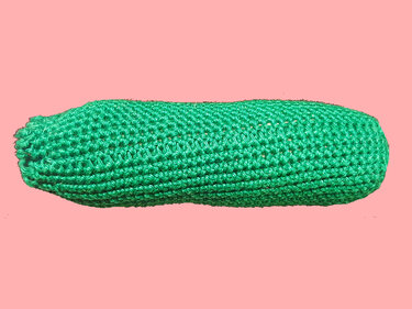 Längliche, grüne gehäkelte Gurke auf rosa Hintergrund.