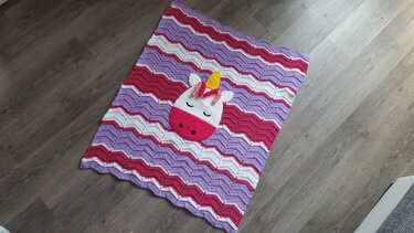 Gehäkelte Babydecke in Rosa, Lila und Weiß mit zentraler Einhorn-Applikation und welligem Ripple-Muster