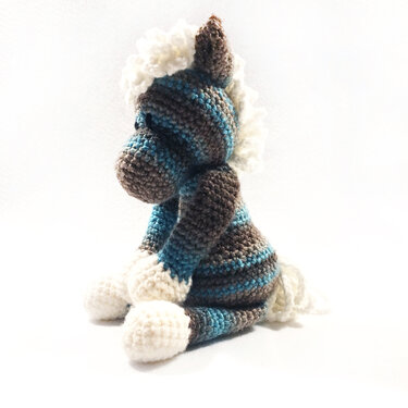 Gehäkeltes gestreiftes Amigurumi in Blau und Braun mit weißer Mähne, seitliche Ansicht