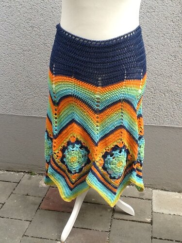 Gehäkelter Rock auf Schaufensterpuppe mit dunkelblauem Bund, Chevron-Streifen in Orange, Türkis und Grün und quadratischen Motiven am Saum.