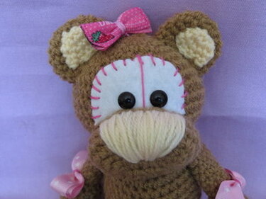 Braun-cremefarbener gehäkelter Amigurumi-Affe mit rosa Schleife und dekorativen Bändern