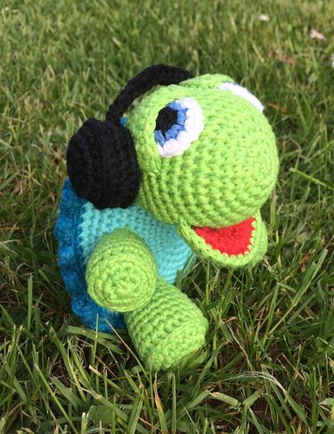 Grüne und blaue gehäkelte Schildkröte mit schwarzen Kopfhörern im Gras