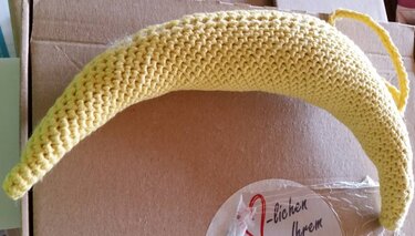 Gelbe gehäkelte Banane mit Aufhängeschlaufe auf braunem Karton