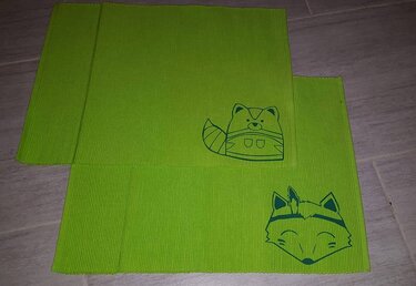 Zwei grüne, gerippte Stoffstücke mit dunklen Umrissmotiven von Fuchs und Waschbär.