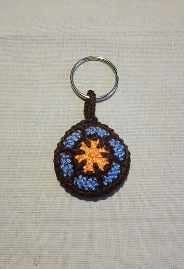 Runder gehäkelter Schlüsselanhänger in Braun, Blau und Orange mit sternförmigem Muster und Metallring
