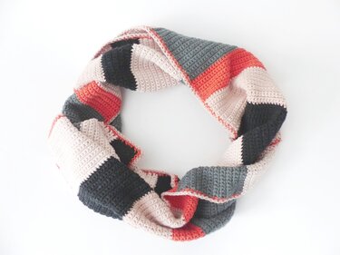 Gehäkelter Loop-Schal in Beige, Grau und Koralle mit Farbblockmuster auf weißem Hintergrund