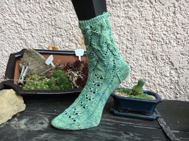 Nahaufnahme einer grünen gestrickten Ankle-Socke mit Ajour- und Zopfmuster auf einem Fußmodell