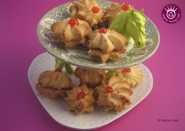 Selbstgemachte zweistöckige Etagere aus zwei Tellern mit grün lackiertem Spielzeugpferdekopf als Stütze, belegt mit kleinen Keksen, vor pinkem Hintergrund