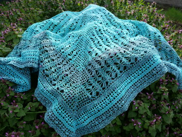 Türkis-blaugrünes, gehäkeltes Dreieckstuch mit filigranem Lochmuster auf grünen Blättern liegend