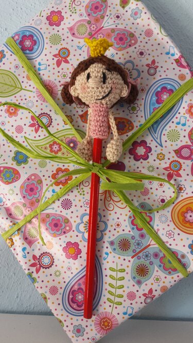 Amigurumi-Prinzessin aus Häkelgarn mit gelber Krone auf rotem Stift, dekorativ an Geschenk gebunden