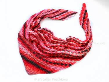 Gehäkeltes Dreieckstuch in Rot-, Rosa- und dunkleren Tönen mit gestreiftem Muster auf hellem Hintergrund