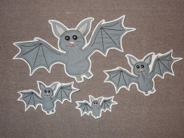 Vier graue Fledermaus-Applikationen in verschiedenen Größen mit weißem Rand auf braunem Textil