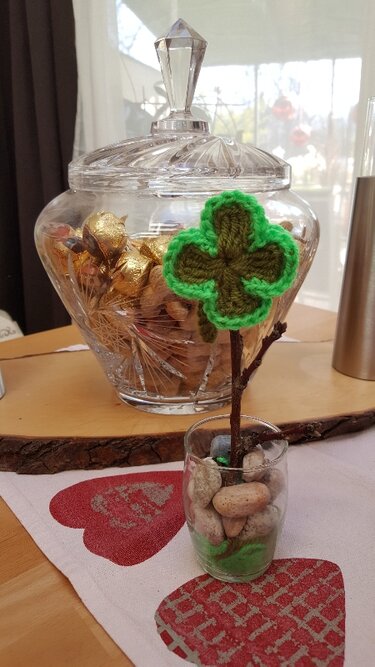 Kleines gehäkeltes vierblättriges Kleeblatt in Grün auf einem Zweig in einem Glas als Dekoobjekt.