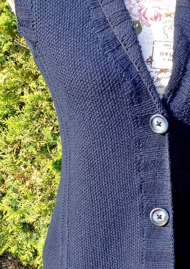 Close-up of navy seed-stitch sleeveless cardigan on a dress form showing V-neck, ribbed button band, and two buttons