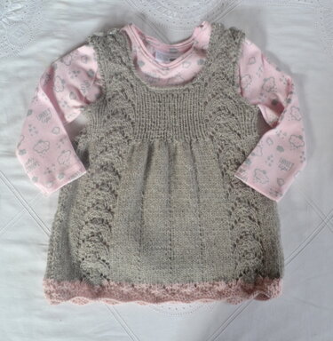 Grau gestricktes Babykleid mit seitlichem Lochmuster und rosa Muschelsaum über rosa Langarmbody