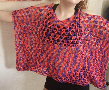 Person trägt gehäkelten offenen Poncho in Orange- und Violetttönen über schwarzem Top