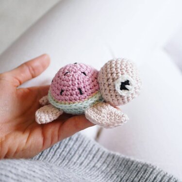 Hand holding small crocheted amigurumi turtle with pink shell and mint trim